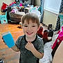 David joined the competition — help win amazing prizes! child, smiling, indoor, clothing, cup, floor, boots, furniture, curtains, window, tattoo, person, hair, face, wooden_floor, box, pile_of_clothes, living_room, happy, casual