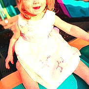 Chloe is registered to the contest to win money with this photo: child, toddler, smiling, red_hair, white_dress, playground, slide, outdoor, sunlight, happy, person, cute, young_child, summer, play, fun, bright, colorful, sitting, portrait