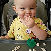 Sophia joined the competition — help win amazing prizes! toddler, child, high_chair, snack, food, pacifier, yellow_shirt, indoor, smile, face, hand, table, baby, cute, happy, eating, seat, playful, young_child, portrait