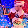 baby, child, christmas, santa_hat, santa_outfit, presents, gift_wrapping, toys, holiday_lights, blue_lighting, indoor, festive, holiday, smiling, hands, face, cute, young_child, celebration, christmas_tree