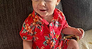 Carter is registered to the contest to win money with this photo: toddler, child, smiling, sitting, red_clothing, floral_pattern, blond_hair, barefoot, couch, blanket, indoor, happy, cute, portrait, person, baby, casual, relaxed, young_child, home