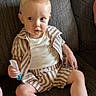 toddler, child, comb, striped_clothing, shorts, shirt, white_tshirt, sitting, couch, brown_couch, indoors, hair, blond_hair, barefoot, curious_expression, person, furniture, young_child, home, portrait