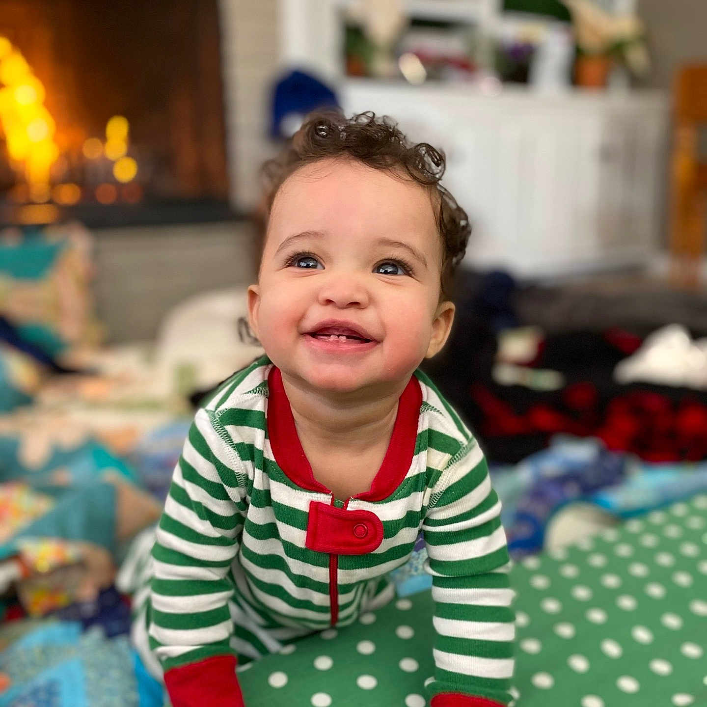 Ariyah joined the competition — help win amazing prizes! baby, child, smiling, pajamas, striped_clothing, indoor, fireplace, cozy, holiday, curly_hair, crawling, polka_dot, cushion, cheerful, portrait, warm_lighting, home_interior, window, furniture, happy