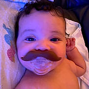 Ariyah is registered to the contest to win money with this photo: baby, pacifier, mustache, close_up, smile, face, curly_hair, blanket, infant, child, skin, lying_down, cute, indoors, portrait, expression, young_child, cheek, hand, comfort