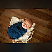 Colton joined the competition — help win amazing prizes! baby, newborn, sleeping, basket, blanket, blue_blanket, wooden_floor, cozy, soft_texture, infant, wrapped, indoors, peaceful, cute, resting, portrait, child, homedecor, warm_tones, knit