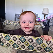 Raelynn joined the competition — help win amazing prizes! baby, child, playpen, smile, happy, indoor, blue_eyes, curly_hair, patterned_fabric, hand, furniture, lamp, cup, blanket, person, portrait, infant, home, cute, grip