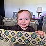 baby, child, playpen, smile, happy, indoor, blue_eyes, curly_hair, patterned_fabric, hand, furniture, lamp, cup, blanket, person, portrait, infant, home, cute, grip