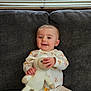 baby, child, pajamas, stuffed_animal, couch, gray_couch, smiling, happy, indoor, window_blinds, knitted_toy, feet, sitting, infant, cute, relaxed, home, soft_toy, childrens_clothing, cozy