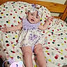 baby, infant, girl, smiling, headband, bow, floral_dress, blanket, polka_dots, bed, wooden_bed, happy, arms_outstretched, milestone, text_overlay, indoor, child, cute, lying_down, portrait