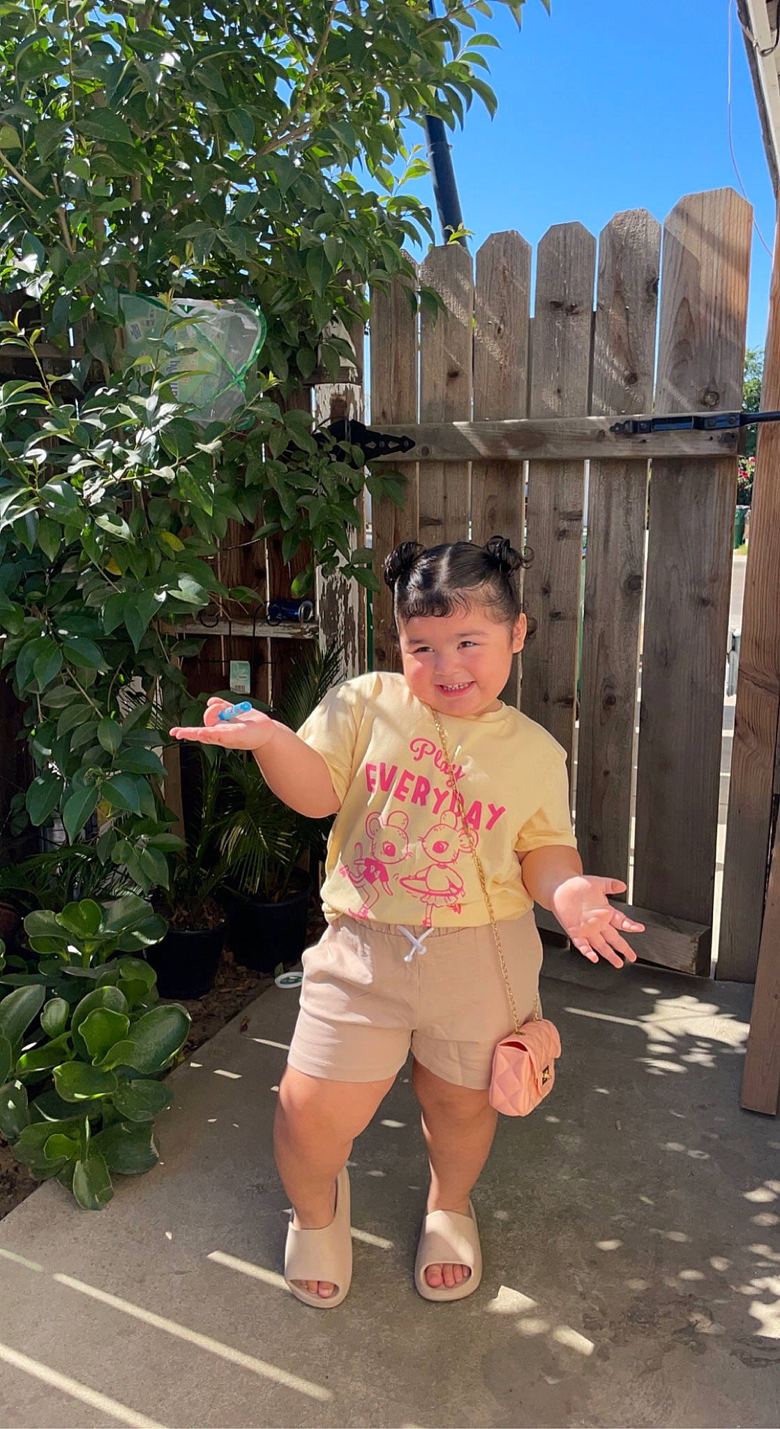 Mia is registered to the contest to win money with this photo: child, fence, fun, garden, grass, happy, home_fencing, human_leg, joy, leisure, person, plant, recreation, sandal, shorts, sky, sleeve, t_shirt, thigh, toddler