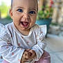 baby, child, smiling, happy, face, blue_eyes, messy, food, white_shirt, pink_hearts, pink_pants, sitting, floor, tiles, indoor, plants, blurred_background, portrait, cute, toddler
