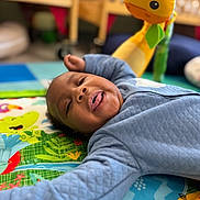 Hayes joined the competition — help win amazing prizes! baby, child, play_mat, toy, giraffe_toy, colorful, nursery, infant, smiling, tongue_out, blue_clothing, quilted_jacket, floor, indoor, crawling_mat, cute, happy, young_child, person, closeup