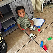 Antoine joined the competition — help win amazing prizes! toddler, child, floor, tiles, blocks, toys, sneakers, green_clothing, cabinet, vase, dried_flowers, indoor, play, curious, messy, expression, person, hair, sitting, red_block