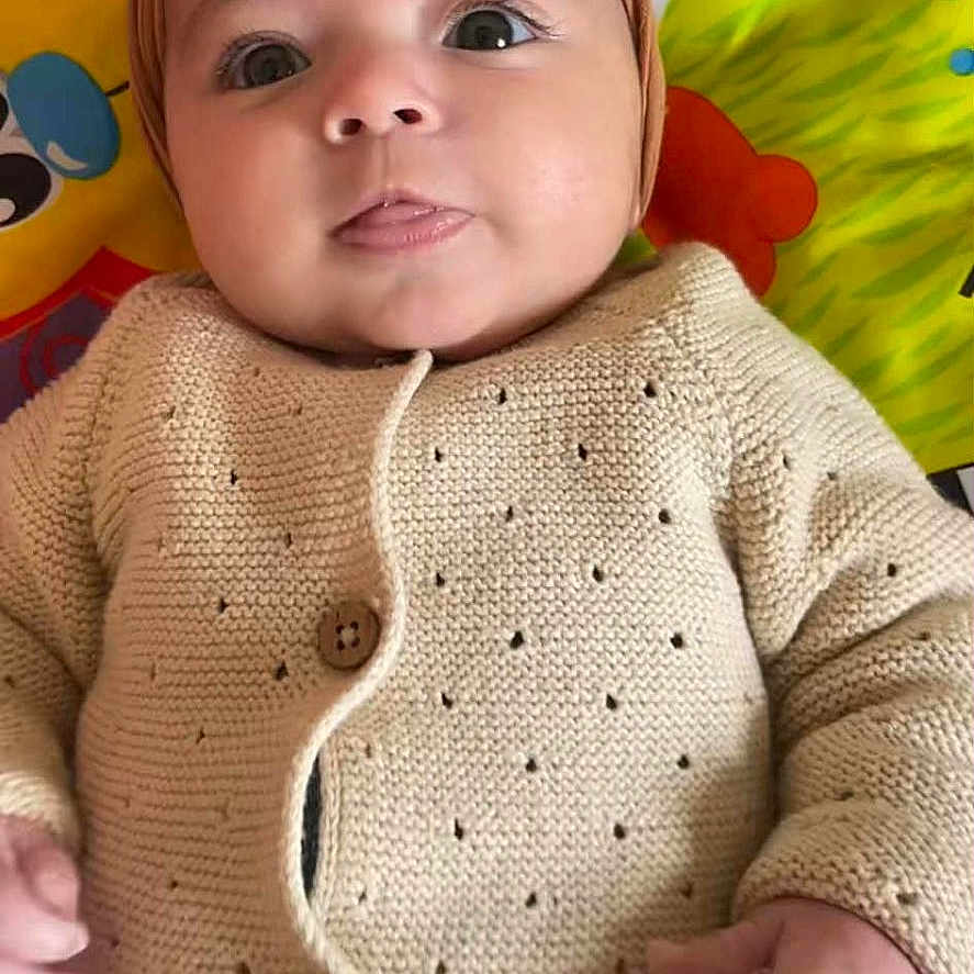 Eline a rejoint le concours — aidez-le/la à gagner de superbes lots ! baby, child, clothing, colorful_background, cute, hand, happy, headband, indoor, infant, knitted_cardigan, laying_down, person, play_mat, pom_pom, portrait, smiling, soft_texture, tongue_out, wide_eyes
