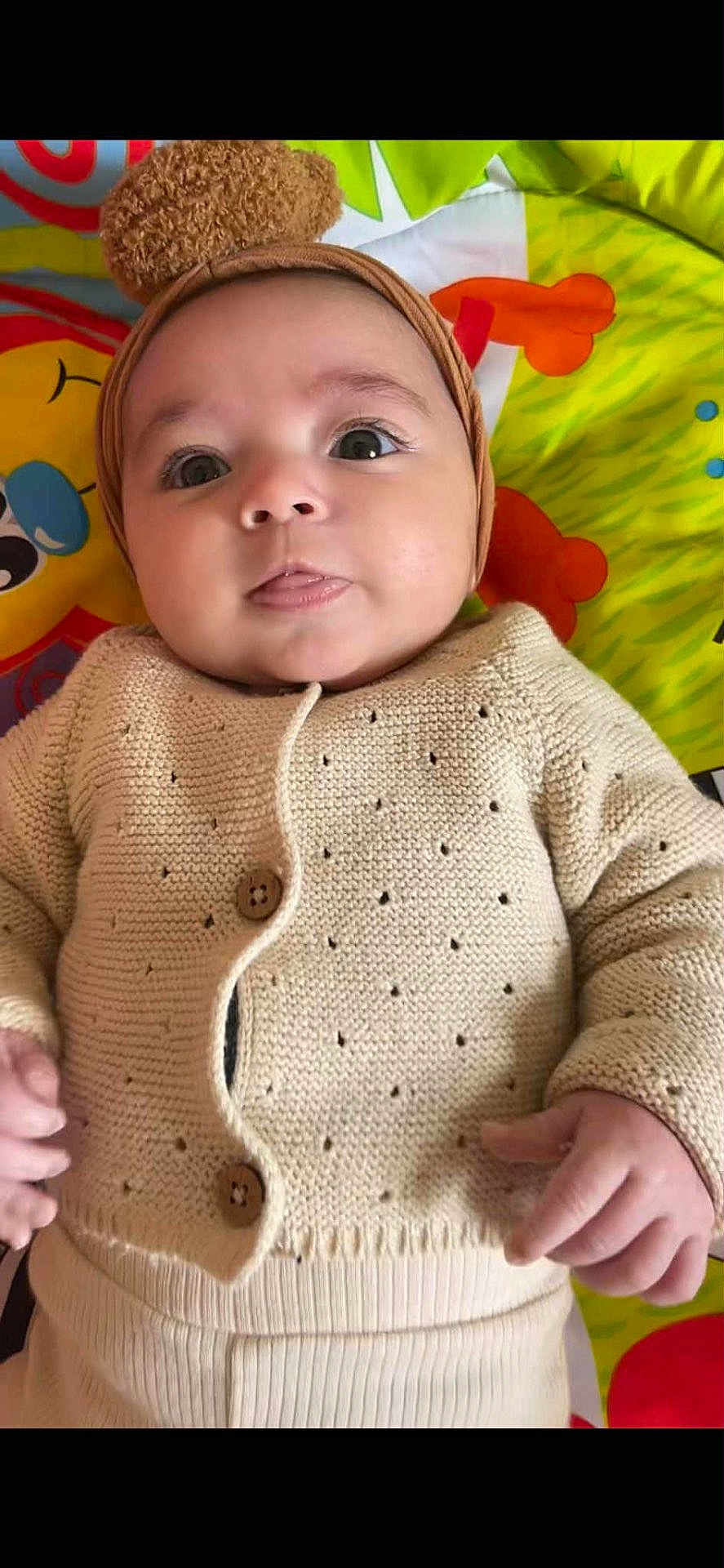 Eline a rejoint le concours — aidez-le/la à gagner de superbes lots ! baby, child, clothing, colorful_background, cute, hand, happy, headband, indoor, infant, knitted_cardigan, laying_down, person, play_mat, pom_pom, portrait, smiling, soft_texture, tongue_out, wide_eyes