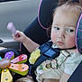 baby, car_interior, car_seat, child, clothing, expression, face, flower_toy, hair, hand, person, pink_trim, safety, seatbelt, sitting, toddler, toy, window, wooden_toy, young_child