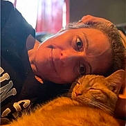 Jinx is registered to the contest to win money with this photo: person, cat, orange_tabby, indoor, cozy, relaxed, smiling, face, pet, sleeping_cat, closeup, warm_light, casual, portrait, human, animal, comfort, resting, cuddle, home