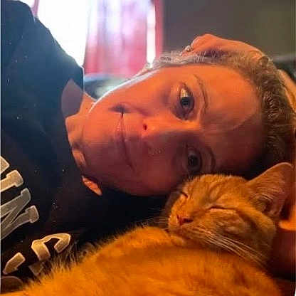 Jinx is registered to the contest to win money with this photo: person, cat, orange_tabby, indoor, cozy, relaxed, smiling, face, pet, sleeping_cat, closeup, warm_light, casual, portrait, human, animal, comfort, resting, cuddle, home