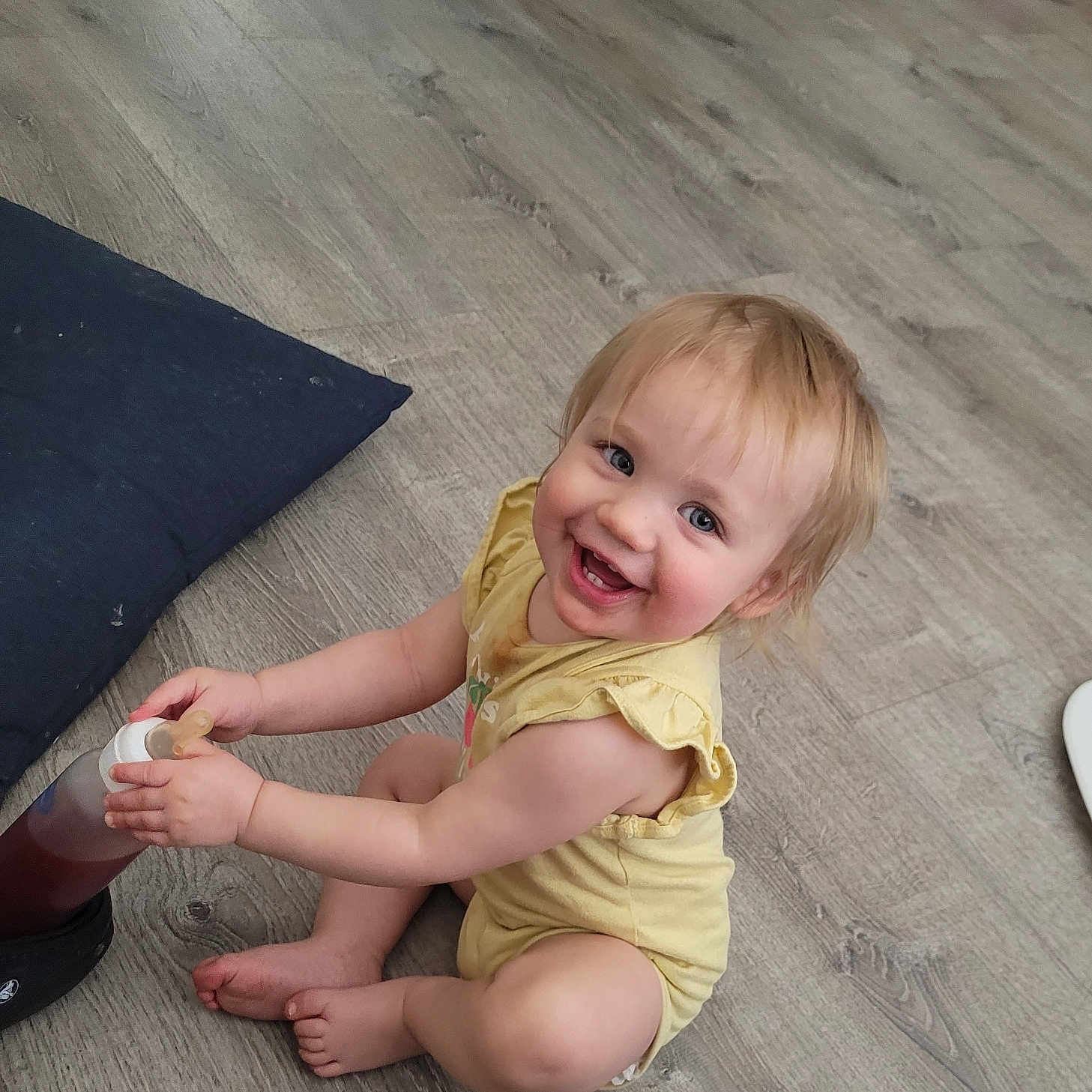 Odysseia is registered to the contest to win money with this photo: baby, bodypart, clothing, couch, dress, face, finger, hand, happy, hardwood, head, laughing, pants, person, photography, portrait, shorts, sitting, smile, wood