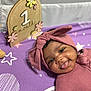 baby, bed, cap, clothing, crib, face, furniture, happy, hat, head, homedecor, indoors, infantbed, person, photography, portrait, purple, quilt, smile, text