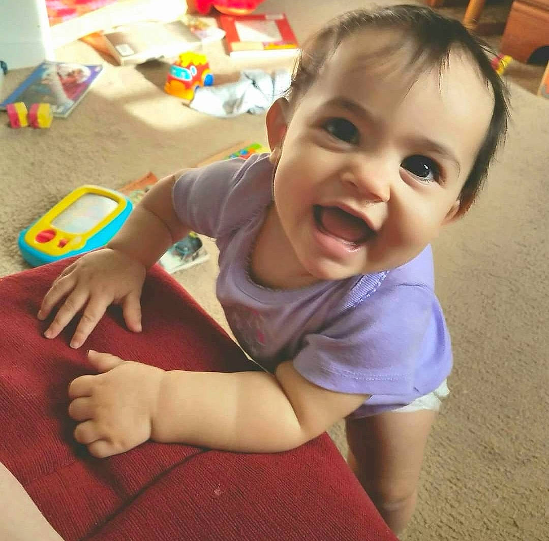 Anya is registered to the contest to win money with this photo: baby, baby_toddler_clothing, cheek, child, clothing, face, finger, floor, flooring, fun, happy, head, human_body, iris, person, skin, sleeve, smile, thumb, toddler