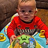 Dailier is registered to the contest to win money with this photo: baby, child, curious, face, floor, furniture, hands, home, indoor, looking, person, plaything, red_clothing, seat, sitting, sofa, toy, walker, wood_floor, young_child