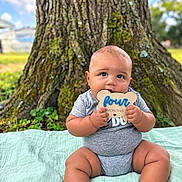 Malaki is registered to the contest to win money with this photo: baby, infant, child, portrait, sitting, smiling, outdoor, tree, moss, blanket, wooden_sign, milestone, eight_months, blue_sky, grass, park, baby_clothing, bare_feet, family_photo, nature