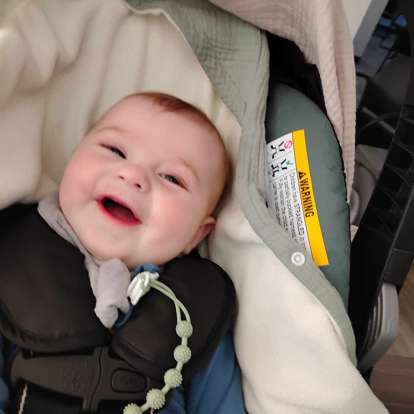 Leelynd is registered to the contest to win money with this photo: baby, beaded_chain, blanket, car_seat, cheeks, closeup, clothing, fabric, face, happy, harness, head, indoor, infant, infant_carrier, pacifier_clip, padding, safety_label, smiling, timestamp
