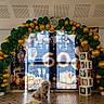 animal, balloon_arch, birthday, blocks, ceiling, celebration, cute, decorations, dog, event, festive, floor_tiles, gift_boxes, gold_balloons, green_balloons, happy, indoor, number_60, party, pets