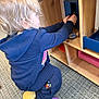 toddler, child, playing, toy, wooden_toy, carpet, indoor, clothing, socks, purple_sock, yellow_sock, hoodie, dollhouse, dolls, furniture, blonde_hair, kneeling, floor, young_child, curly_hair