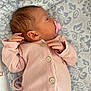 baby, newborn, infant, pacifier, pink_clothing, ribbed_fabric, buttoned_onesie, lying_down, blanket, patterned_blanket, soft_texture, sleepy, cute, newborn_baby, infant_face, small_hands, baby_clothes, indoors, resting, calm