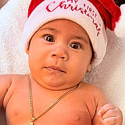 Angelo joined the competition — help win amazing prizes! baby, infant, santa_hat, christmas, holiday, necklace, gold, dragon, bare_chest, cute, portrait, expression, fist, skin, indoors, blanket, festive, headwear, holiday_season, celebration