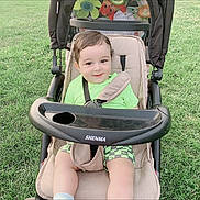 Yassine joined the competition — help win amazing prizes! toddler, child, stroller, grass, outdoor, green_clothing, smile, baby, seatbelt, sunlight, toy, happy, portrait, cute, sitting, person, playful, nature, daylight, casual