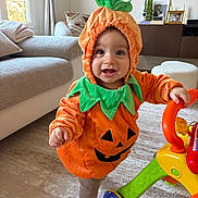 Joseph participe au concours pour gagner de l'argent avec cette photo : baby, toddler, child, pumpkin_costume, halloween, smile, indoor, living_room, toy, walker, couch, rug, playful, costume, cute, portrait, furniture, hood, eyes, hands