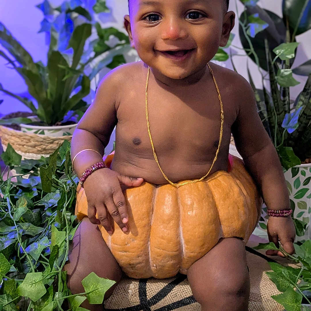 Aro a rejoint le concours — aidez-le/la à gagner de superbes lots ! baby, bracelets, child, closeup, cute, dark_skin, decor, gold_necklace, greenery, happy, indoor, jewelry, leaves, plants, portrait, pumpkin, short_hair, sitting, smiling, sock