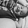 Thomas is registered to the contest to win money with this photo: child, smiling, face, blanket, bed, happy, curly_hair, tshirt, lying_down, portrait, indoors, cute, resting, comfort, young, person, black_and_white, relaxed, expression, cozy