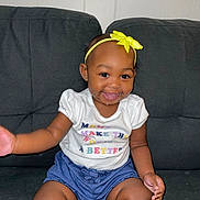 Kyleigha joined the competition — help win amazing prizes! baby, child, smiling, headband, yellow_bow, white_shirt, blue_shorts, drool, sitting, couch, indoor, happy, cute, person, toddler, skin, face, hand, legs, infant