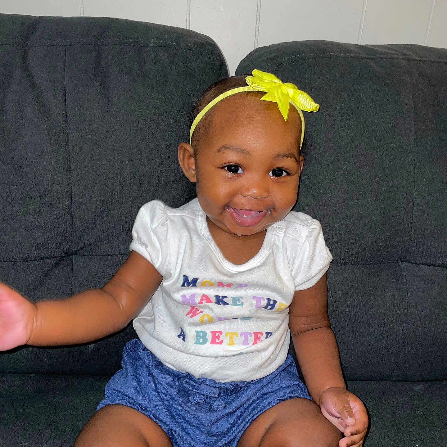 Kyleigha joined the competition — help win amazing prizes! baby, blue_shorts, child, couch, cute, drool, face, hand, happy, headband, indoor, infant, legs, person, sitting, skin, smiling, toddler, white_shirt, yellow_bow
