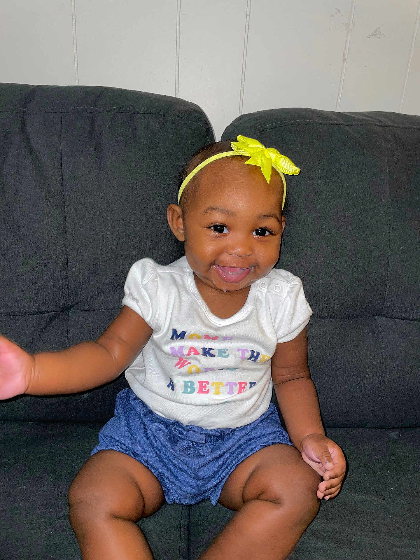 Kyleigha joined the competition — help win amazing prizes! baby, child, smiling, headband, yellow_bow, white_shirt, blue_shorts, drool, sitting, couch, indoor, happy, cute, person, toddler, skin, face, hand, legs, infant