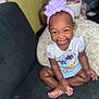 Kyleigha is registered to the contest to win money with this photo: baby, child, clothing, couch, cross_legged, cute, happy, headband, home, indoor, infant, person, pillow, portrait, purple_flower, shirt, shorts, sitting, smiling, toddler