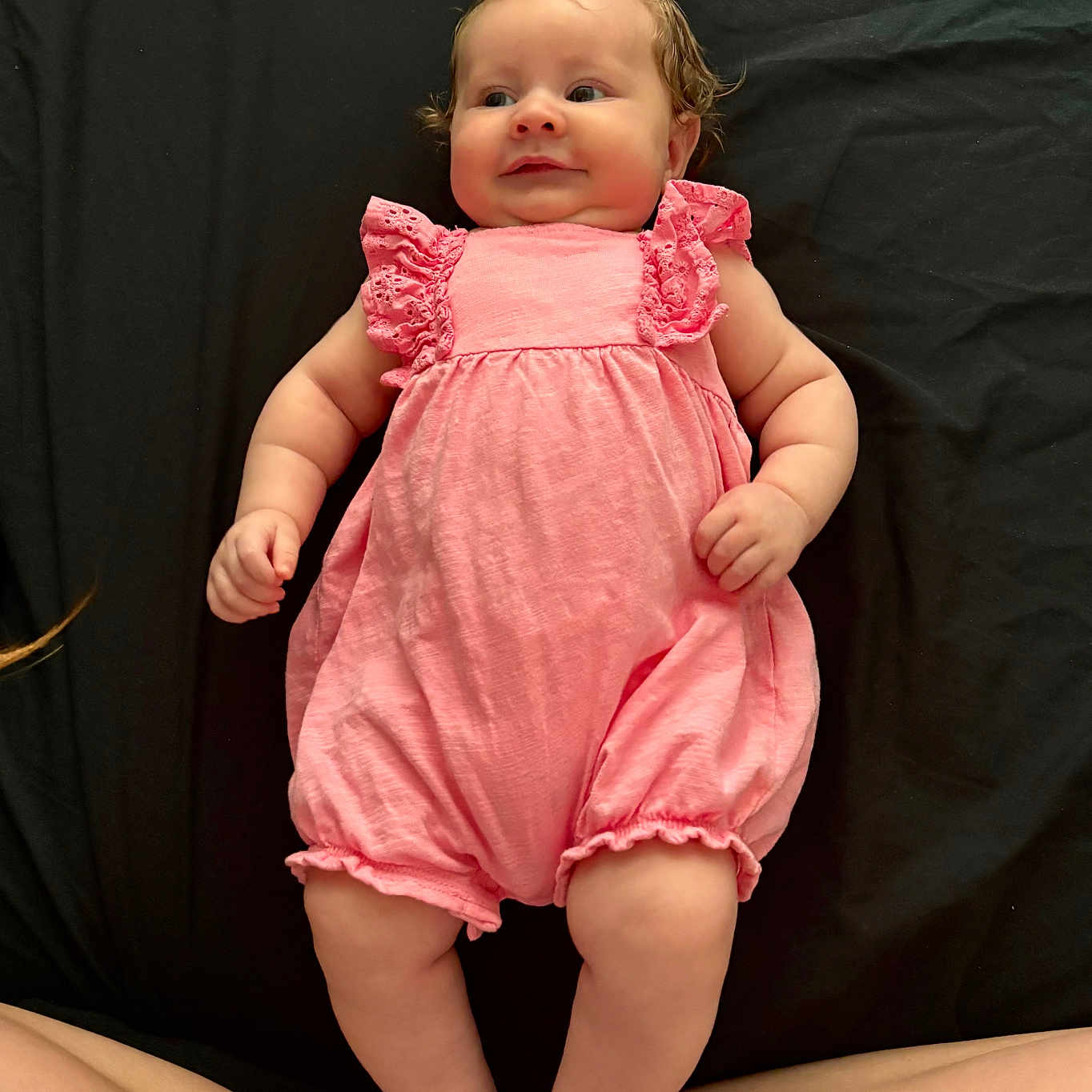 Lyra joined the competition — help win amazing prizes! baby, infant, pink_romper, lying_down, curious_expression, barefoot, skin, legs, adult_legs, child, cute, chubby_cheeks, portrait, indoors, soft_lighting, black_background, person, smile, young_child, one_person