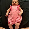 Lyra is registered to the contest to win money with this photo: baby, infant, pink_romper, smiling, lying_down, legs, feet, skin, cute, child, portrait, indoor, person, clothing, happy, young_child, baby_girl, curly_hair, flesh_tone, relaxing