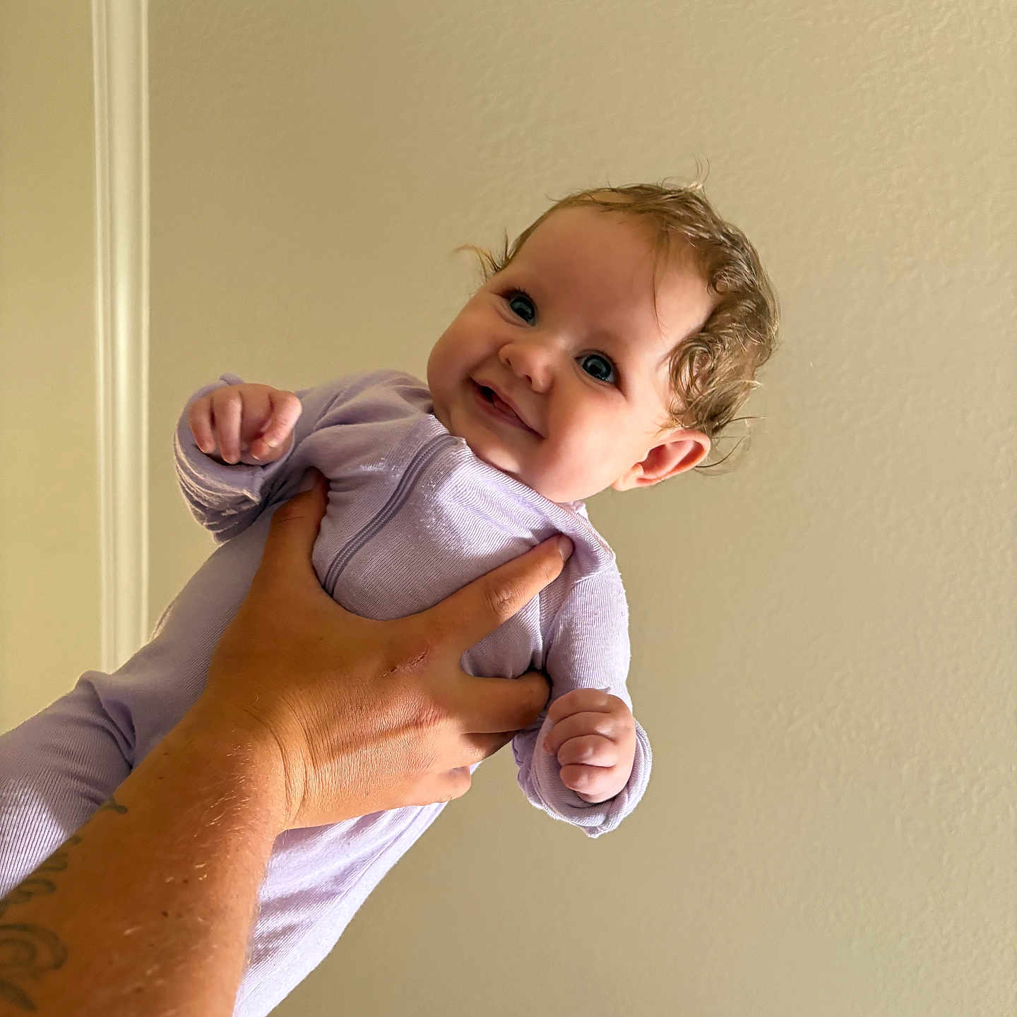 Lyra joined the competition — help win amazing prizes! baby, child, infant, hand, tattoo, onesie, lavender, smile, curly_hair, indoor, wall, person, cute, portrait, skin, fingers, happy, holding, playful, young