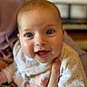Lou participe au concours pour gagner de l'argent avec cette photo : adorable, adult_hand, baby, bib, bokeh, cheeks, close_up, eyelashes, eyes, face, hand, happy, indoor, infant, mouth, onesie, portrait, shallow_depth_of_field, skin, smiling