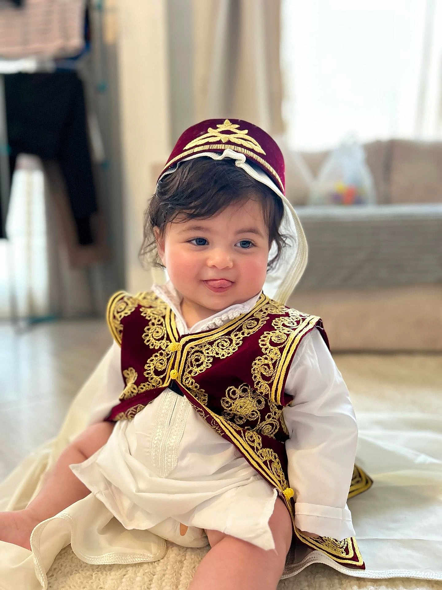 Kaylan participe au concours pour gagner de l'argent avec cette photo : baby, child, traditional_clothing, vest, hat, indoor, sitting, cute, tongue_out, embroidered, white_clothing, soft_surface, blurred_background, smiling, person, infant, headwear, candid, portrait, happy