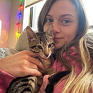 Theo joined the competition — help win amazing prizes! woman, kitten, cat, pet, couch, indoor, cozy, snuggling, casual_clothing, window, string_lights, relaxed, young_adult, home, comfort, hand, long_hair, tabby, feline, portrait