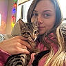 woman, kitten, cat, pet, couch, indoor, cozy, snuggling, casual_clothing, window, string_lights, relaxed, young_adult, home, comfort, hand, long_hair, tabby, feline, portrait