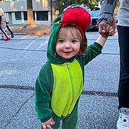 Zaydin is registered to the contest to win money with this photo: toddler, child, costume, dinosaur, green, hood, smile, holding_hands, adult, outdoor, pavement, building, tree, daylight, shoes, cute, happy, person, clothing, casual
