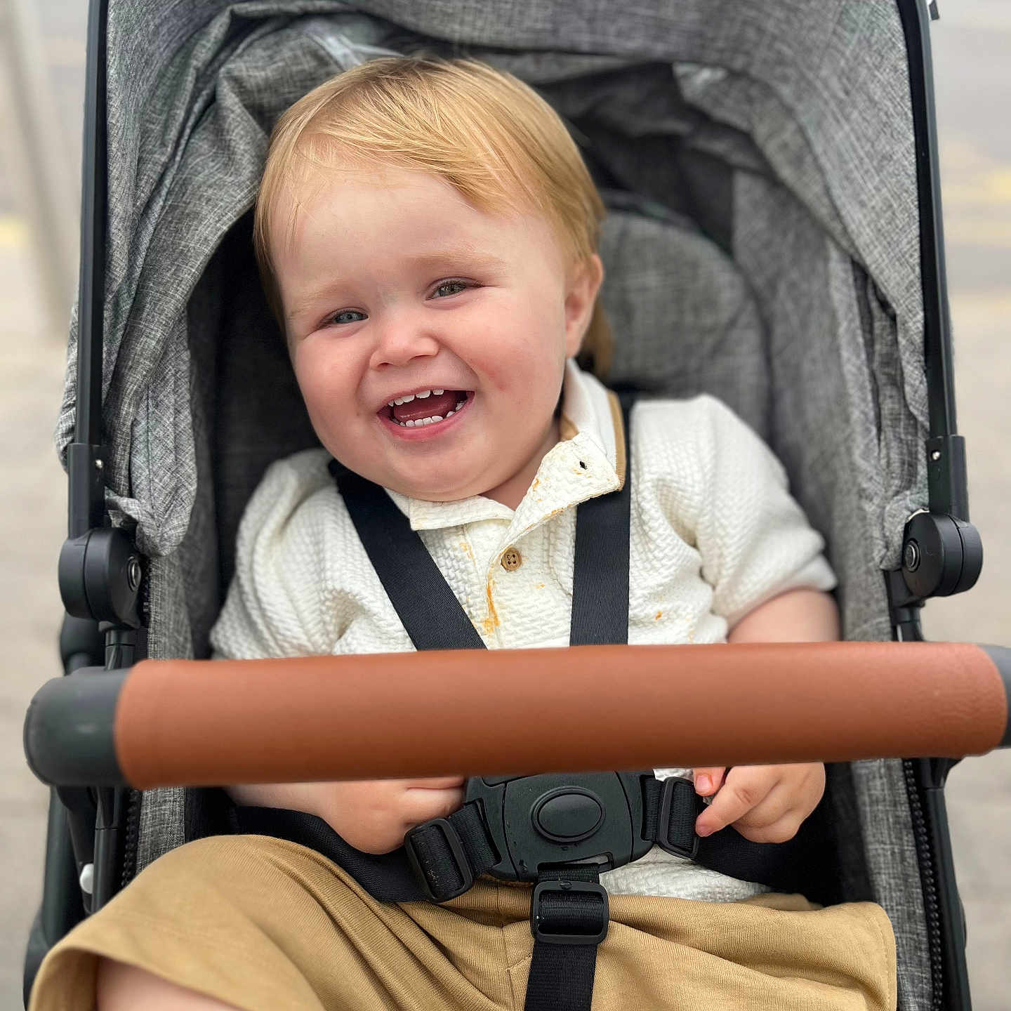 Theo is registered to the contest to win money with this photo: baby, baby_stroller, beige_shorts, blonde_hair, casual_clothing, child, childhood, cute, daytime, happy, outdoor, person, portrait, seat, seatbelt, smiling, stroller, toddler, urban, white_sweater