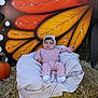 baby, child, pink_clothing, headband, blanket, hay_bale, pumpkin, outdoor, autumn, butterfly_wing, plant, greenery, nature, cute, smiling, portrait, seasonal, fall, sitting, decor